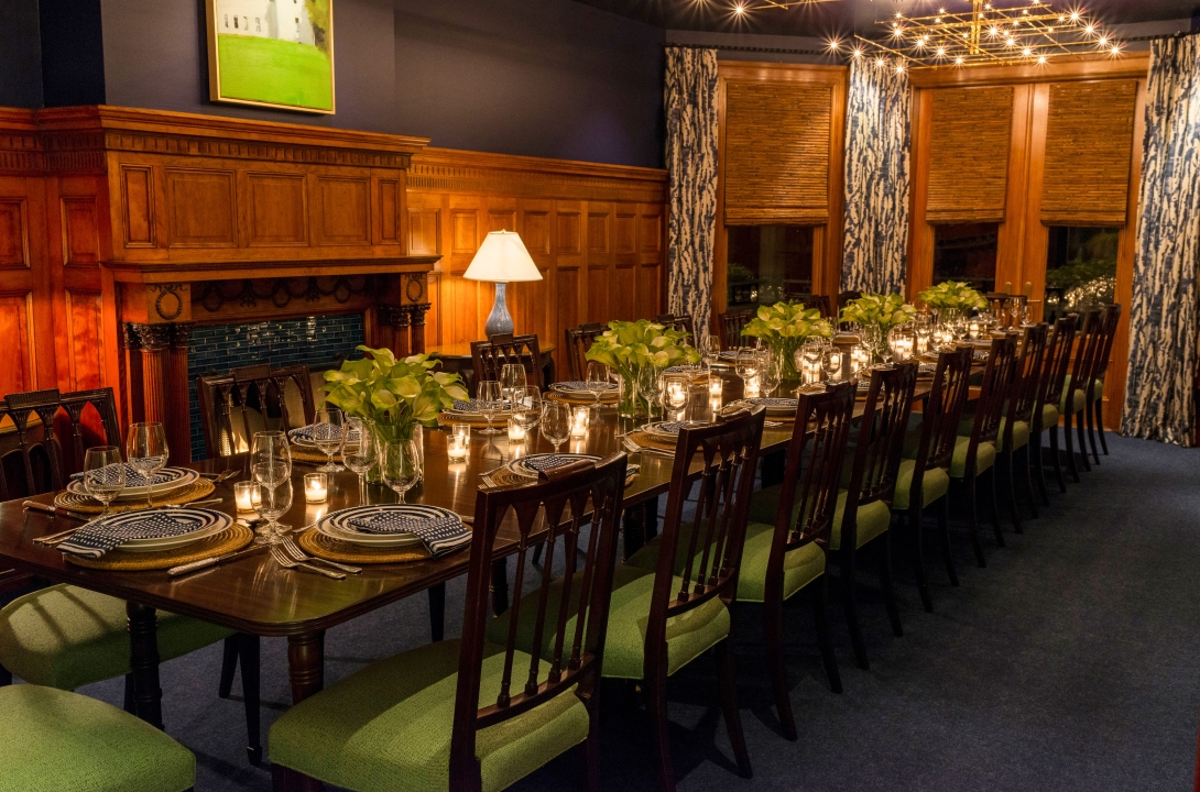 Rowland House dining room with a long table, green chairs, and fireplace.