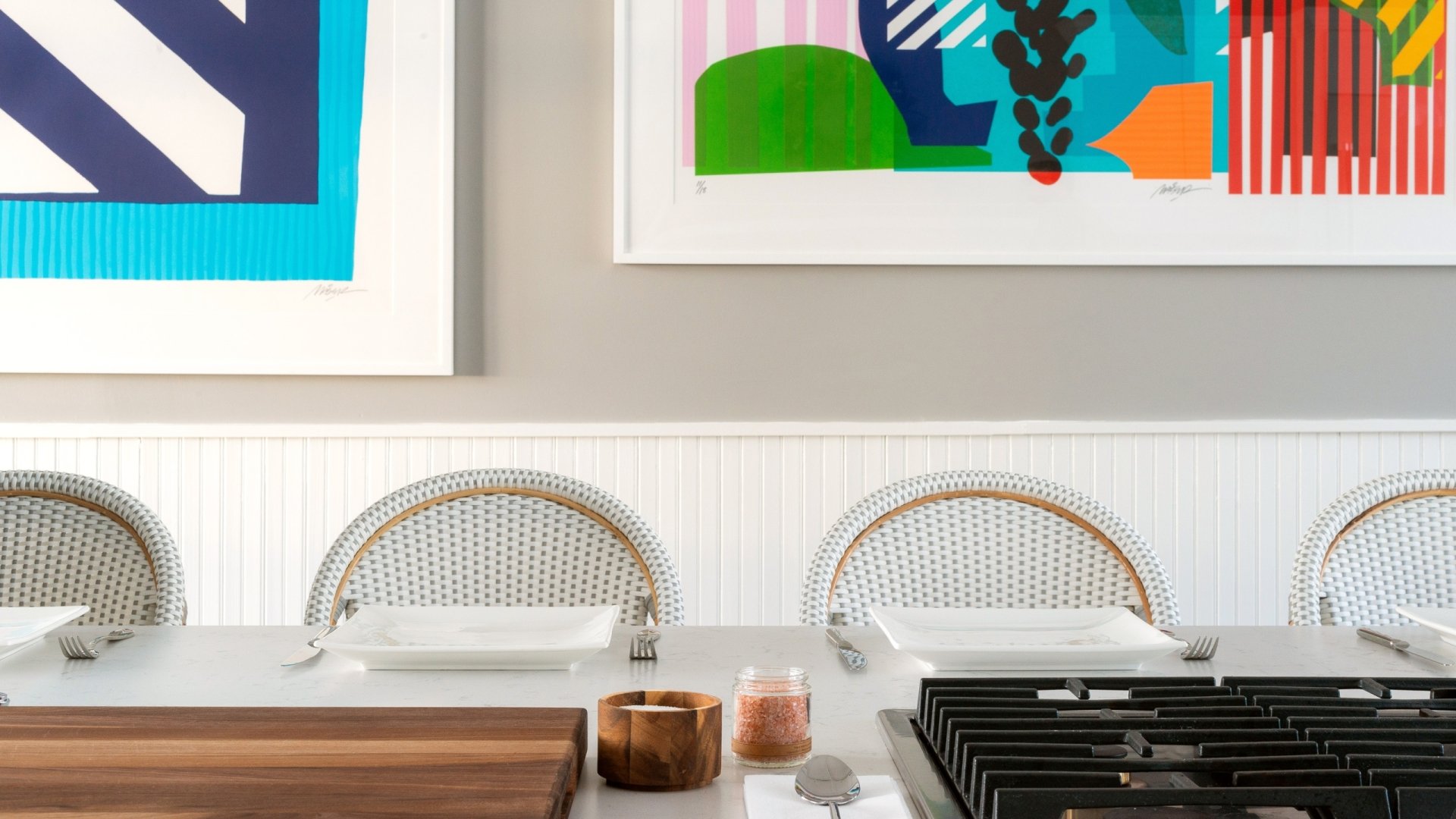 A white table surrounded by white chairs and painting on the wall.