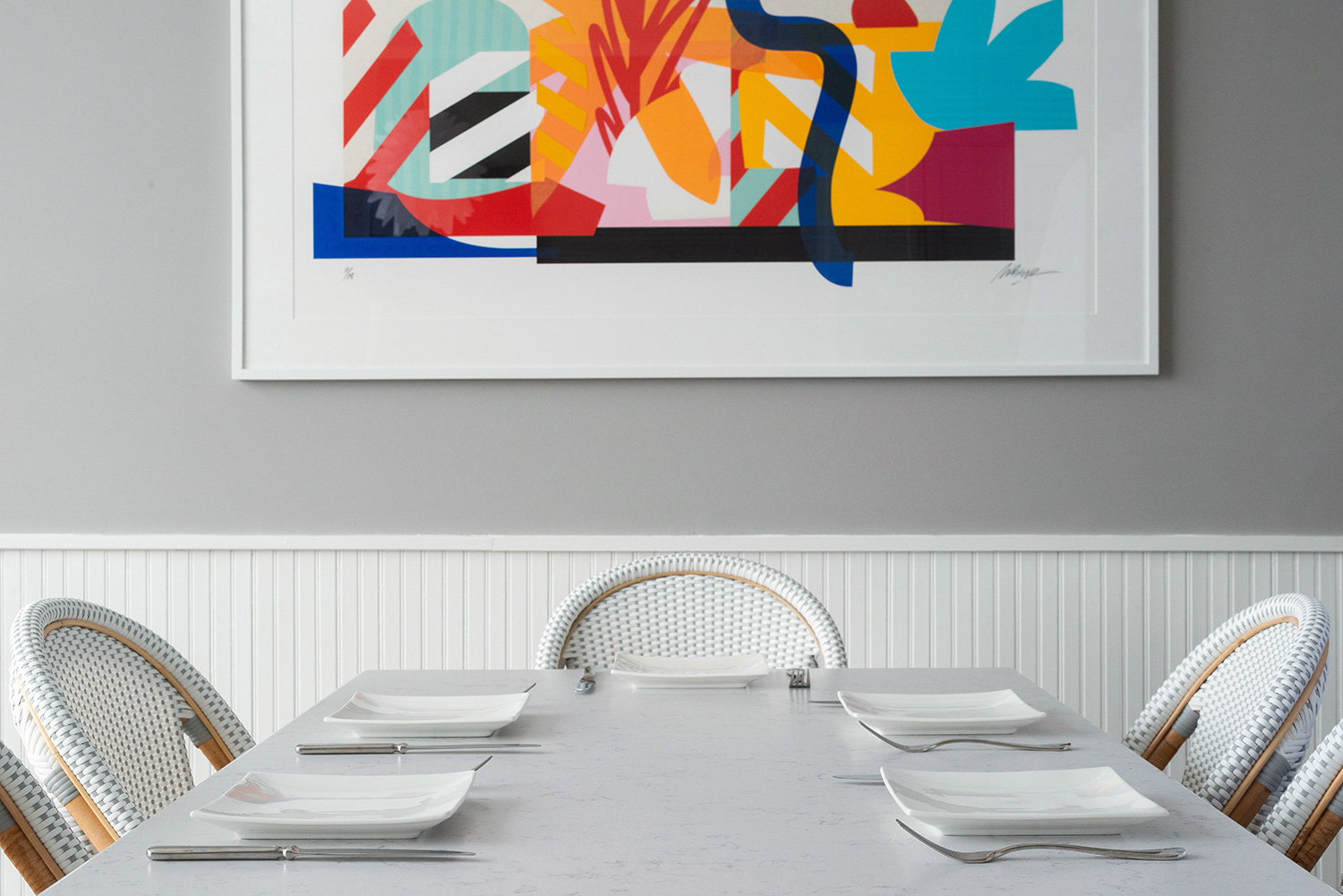 White chairs and dining table in front of colourful painting.
