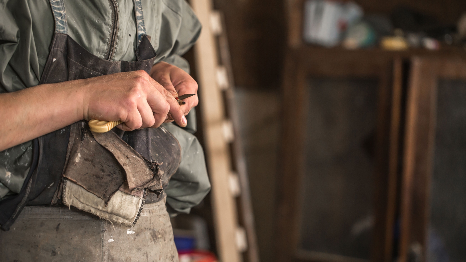 A person in a work apron holding wood carving tool.