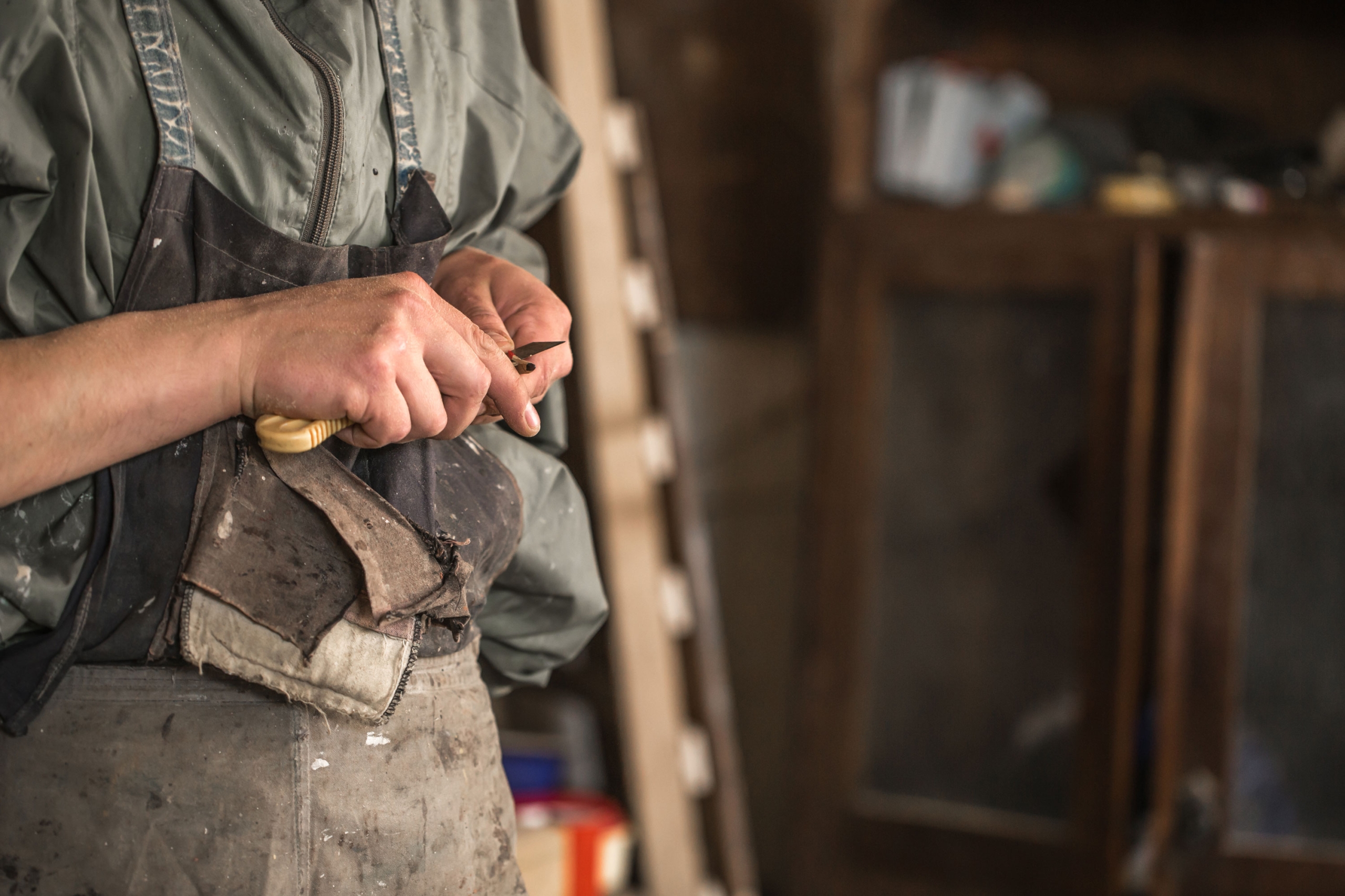A person in a work apron holding wood carving tool.