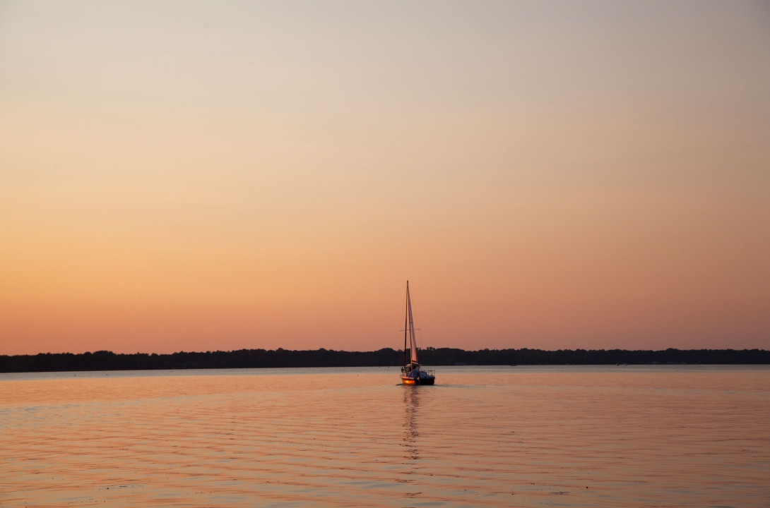 A sailboat on the water as the sun sets in the background.