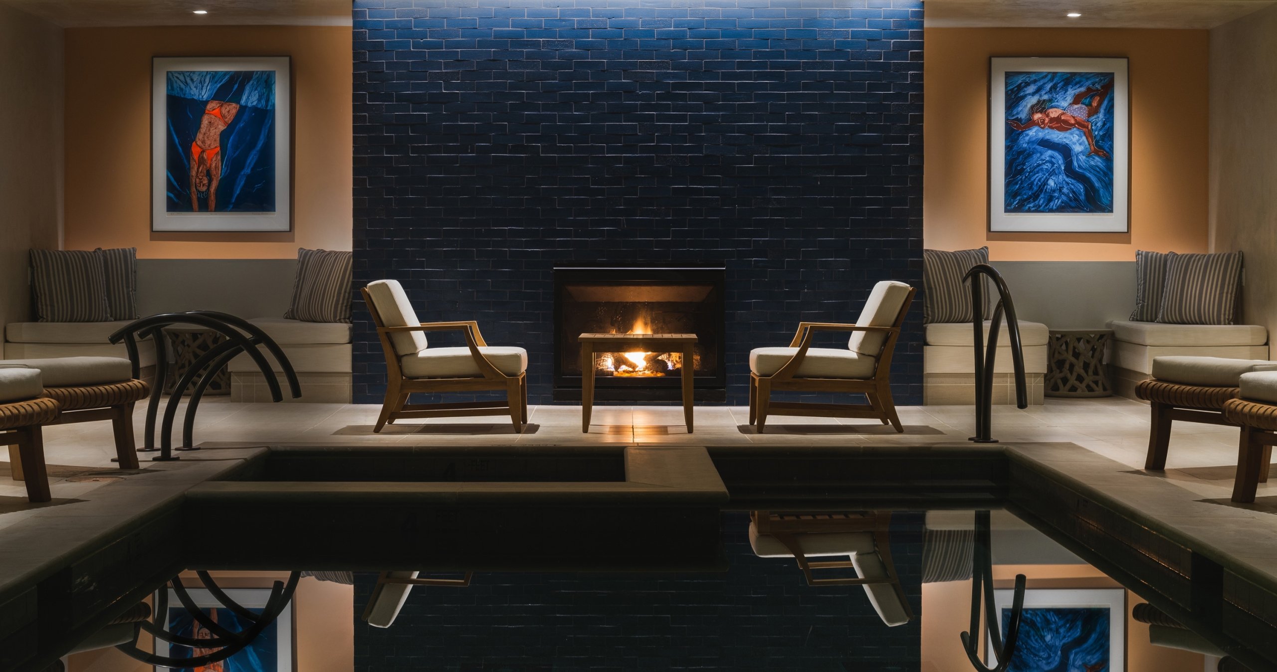 Pair of chairs in front of fireplace and pool in The Spa.