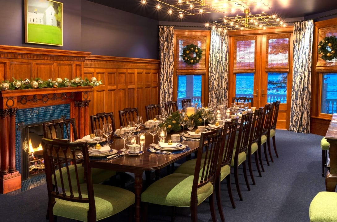 A spacious room with a long table, green chairs and fireplace.