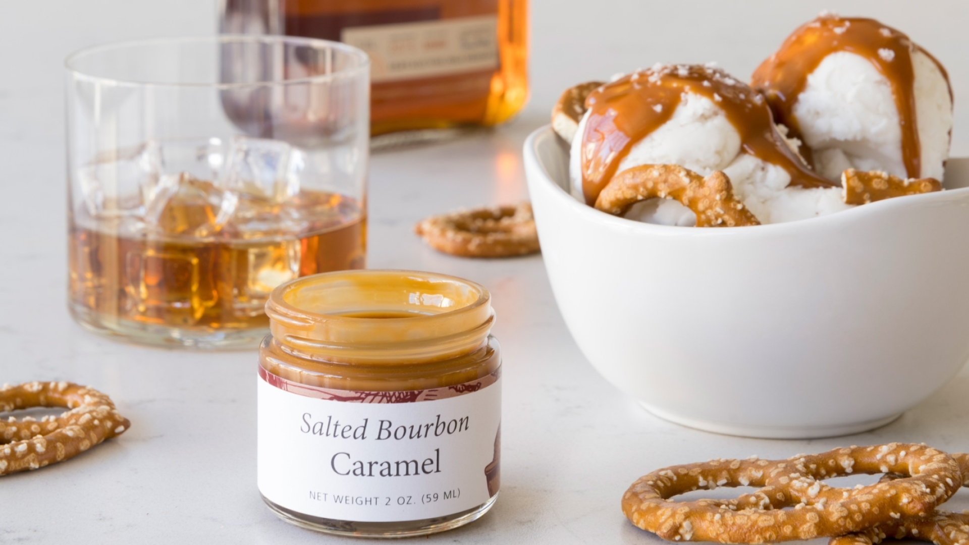 A bowl of pretzels and a bottle of whiskey paired with a Salted Bourbon Caramel Sundae.