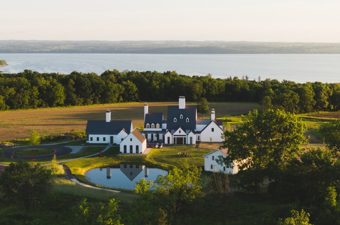 Grand white house on hill with picturesque aerial view of pond.