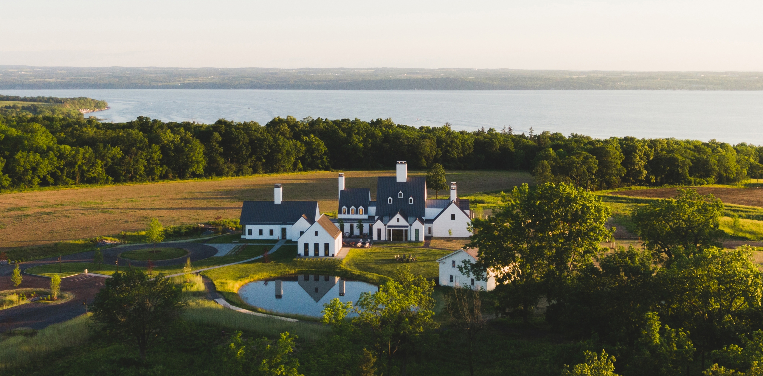 Grand white house on hill with picturesque aerial view of pond.